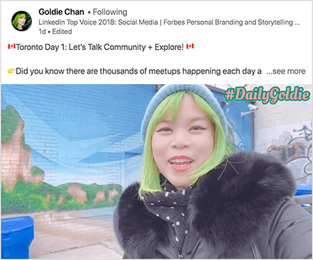 Toto je screenshot z videa LinkedIn, na ktorom Goldie Chan dokumentuje svoje cesty. Text nad videom hovorí: „Toronto Day 1: Let’s Talk Community + Explore! Vedeli ste, že sa každý deň konajú tisíce stretnutí?.. pozrieť viac". Video zobrazuje Goldie pred nástennou maľbou na tehlovej stene. Nástenná maľba zobrazuje jasne modrú oblohu a hnedé útesy pokryté jasnou zeleňou. Goldie sa objaví od hrude hore. Je to ázijská žena so zelenými vlasmi. Na sebe má modrú pletenú čiapku a čiernu bundu s chlpatým golierom. V pravom hornom rohu videa sa #DailyGoldie zobrazuje v broskyňovom texte so zeleným obrysom.